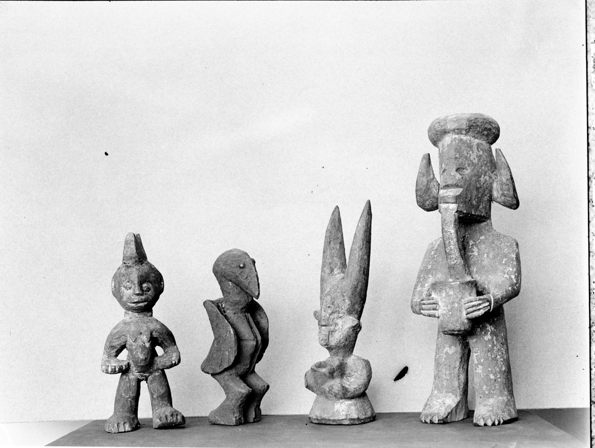 Four carved wooden Agwu Nsi figures of varying forms, including humanoid and avian shapes.