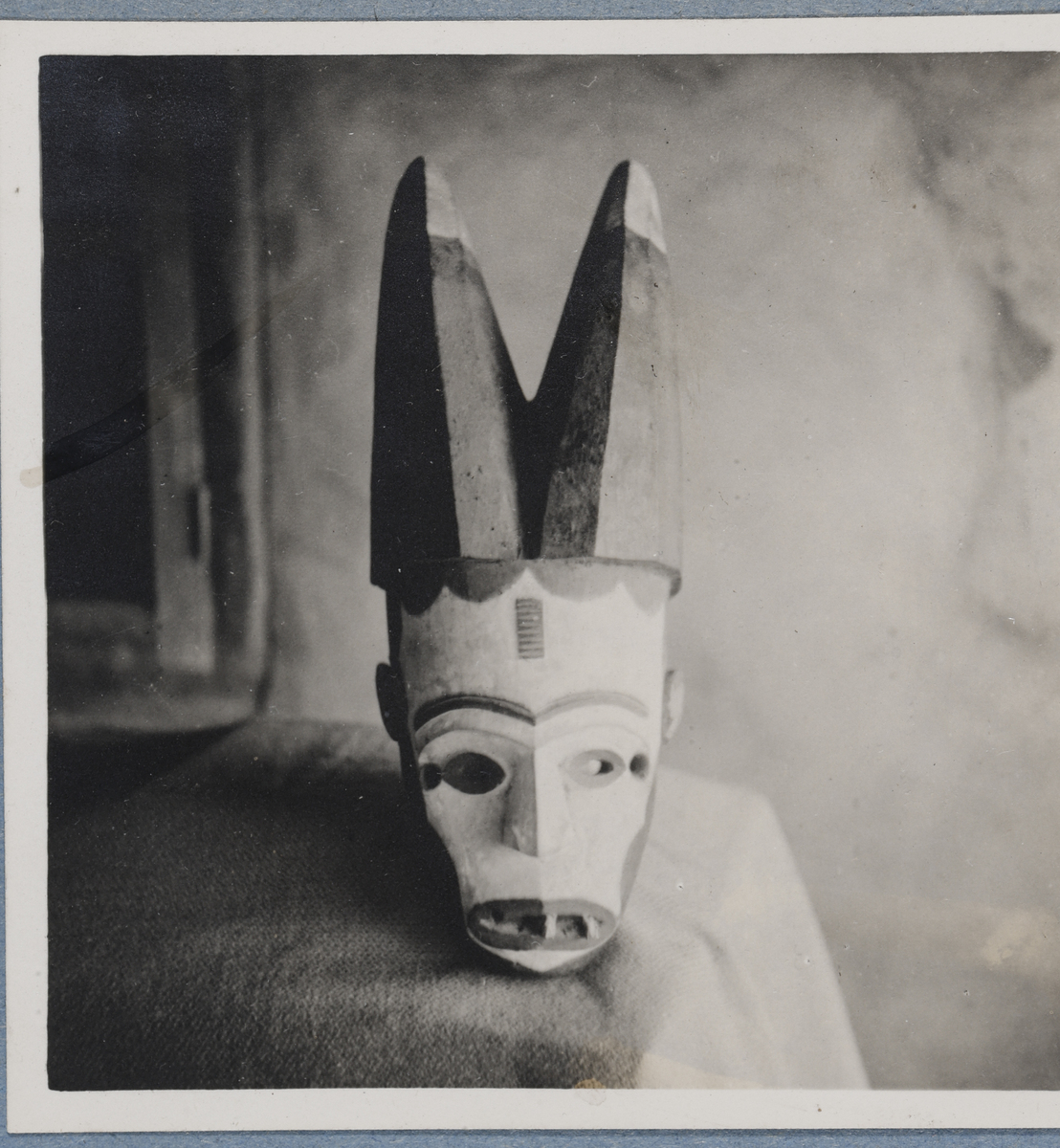 A white wooden face mask with black horns and itchi scarification on the forehead.