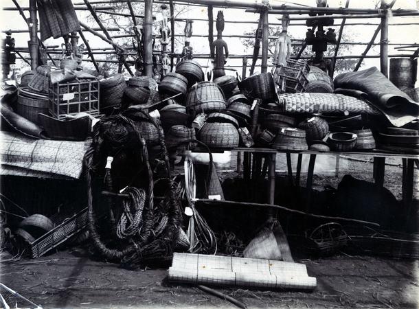 A photograph showing an exhibition stall with hanging carved figures, woven baskets, and ropes under a wooden frame.