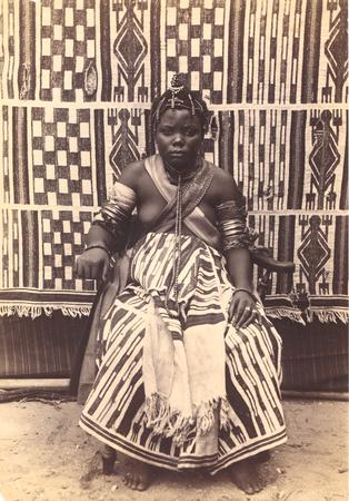 Young adult female in traditional wedding attire seated against a geometric textile backdrop.