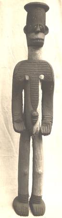 A photograph of a carved wooden Igbo male figure with a flat-top headdress and ribbed torso patterns.