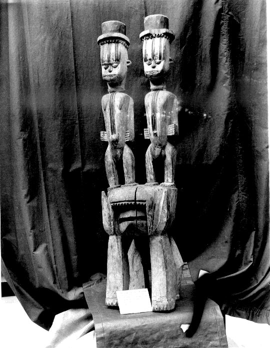 A photograph of a multi-tiered carved wooden shrine object featuring two anthropomorphic figures.