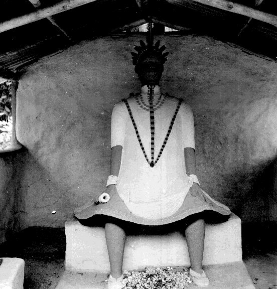 A seated chief of North Ika in ceremonial dress with a radial headpiece and bell-shaped garment.