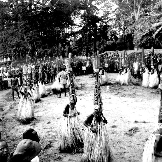Group of masqueraders with tall headdresses and raffia skirts dancing during a boys' initiation in Nkporo.