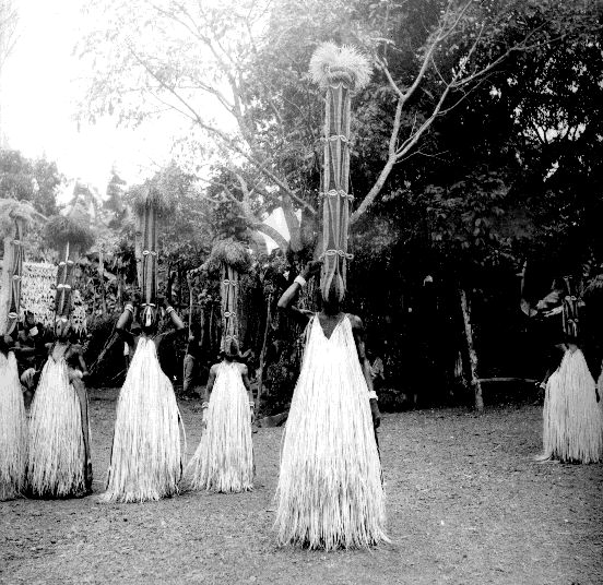 Young male initiates wearing tall cylindrical headdresses and raffia skirts during a ceremony.