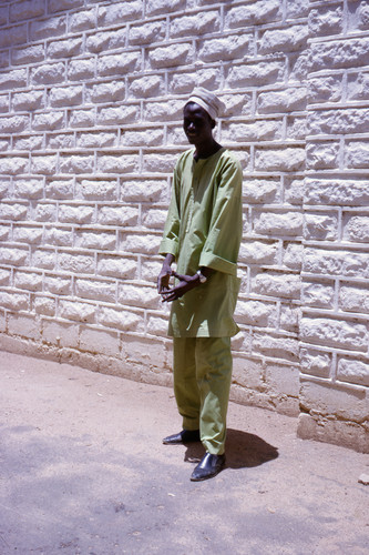 Full-length portrait of an Igbo man in light green tunic and trousers with a white cap.