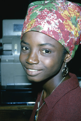 Portrait of a young Igbo woman wearing a multicolored head wrap and burgundy garment.